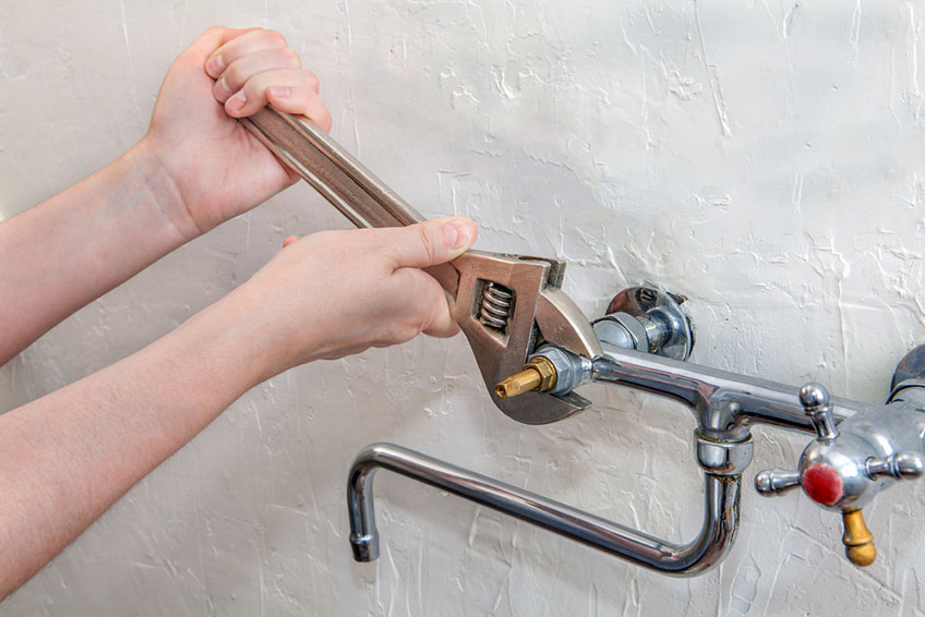 Person turning a monkey wrench on a pipe