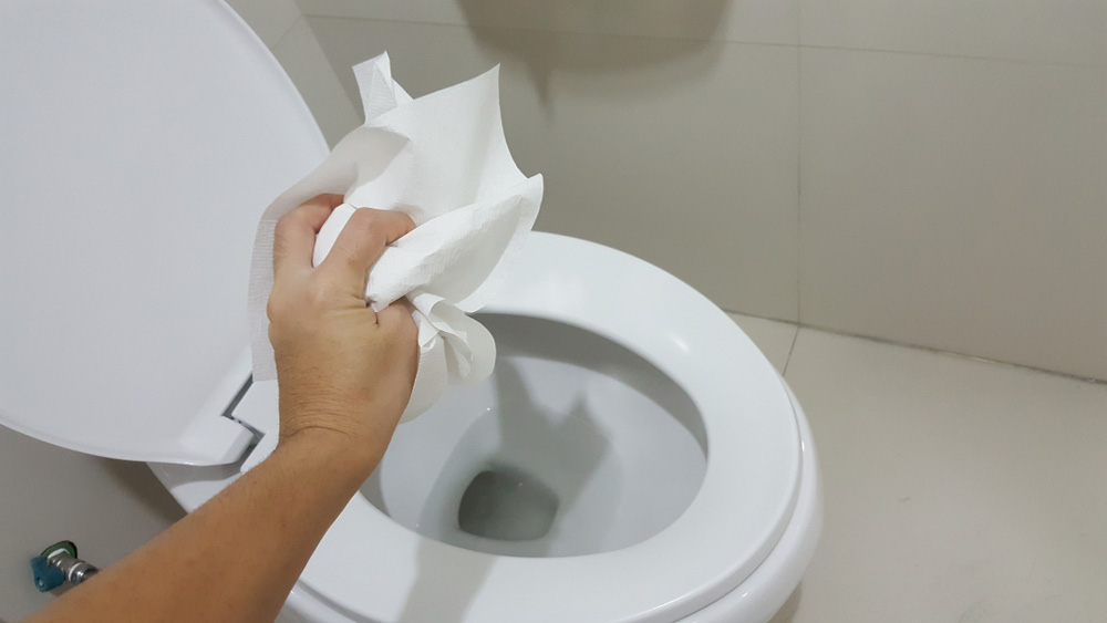 Hand throwing tissue paper directly in the toilet bowl
